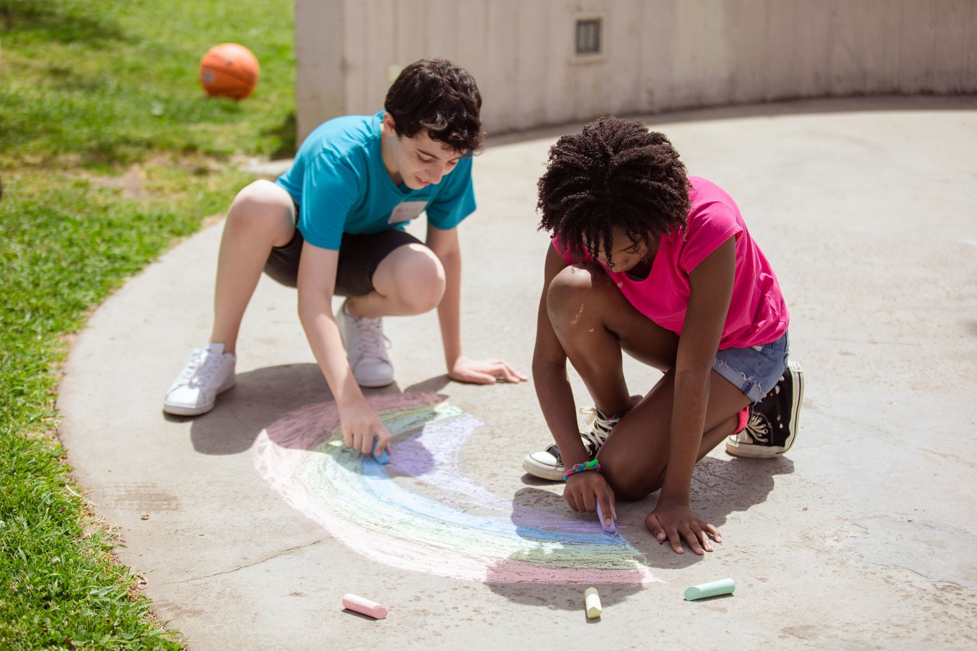 Two kids drawing a chalk rainbow on a clean concrete path