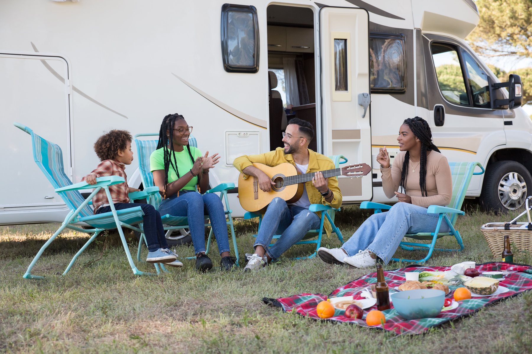 A family on camp chairs beside their motorhome, one playing guitar
